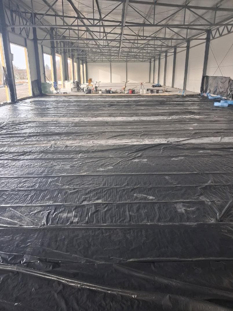 Przygotowanie hali stalowej — czarna folia ochronna, zbrojenie i sprzęt budowlany